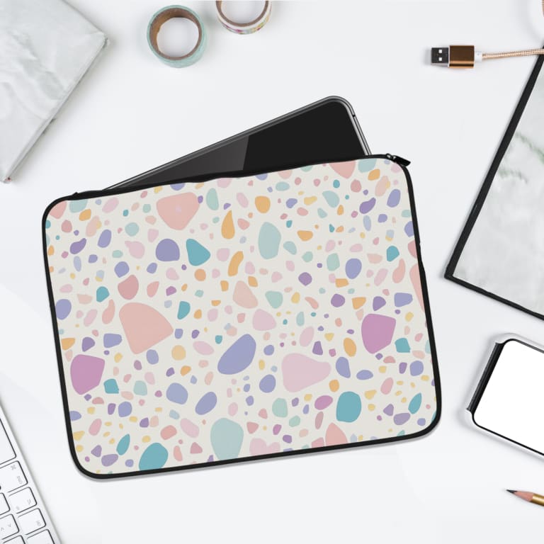 Terrazzo-style laptop sleeve with colorful spots in pink, blue, orange, and purple on a white background, surrounded by a notebook and pen. laptop sleeve kept on a plain white background