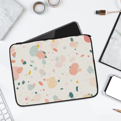 Pastel terrazzo-style laptop sleeve with pink, yellow, blue, and gray shapes on a light background, displayed with desk items like a notebook. laptop sleeve kept on a plain white background