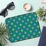 Playful pastel polka dot design laptop sleeve with yellow, purple, and orange dots on a teal background. the laptop sleeve on the table