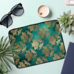 Elegant floral teal-blue laptop sleeve with beige and gold flowers, offering stylish protection for your laptop. the laptop sleeve on the table