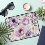 Infidu Elegant Purple Floral Laptop Sleeve featuring large purple flowers and green leaves on a light-colored background. the laptop sleeve on the table