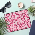 Infidu Pink Heart Pattern Laptop Sleeve with a playful design of large, evenly spaced pink hearts on a light pink background. the laptop sleeve on the table