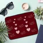 Infidu Maroon Heart & Angel Pattern Laptop Sleeve with white hearts and angel figures on a maroon background. the laptop sleeve on the table