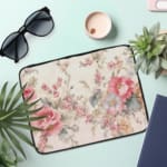 Vibrant pink floral laptop sleeve with large flowers, smaller blooms, and green leaves, offering stylish and elegant protection for your laptop. the laptop sleeve on the table