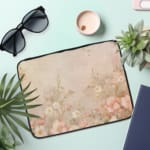 Beige laptop sleeve with subtle floral pattern, featuring a zip closure for secure protection. the laptop sleeve on the table