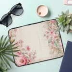 Soft beige laptop sleeve with delicate floral design in pink, green, and purple, featuring a zip closure for secure storage. the laptop sleeve on the table