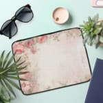 Soft beige laptop sleeve with delicate floral design in pink, green, and purple, featuring a zip closure for secure storage. the laptop sleeve on the table