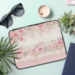 Floral laptop sleeve with pink and white flowers, black-bordered edges, soft background, and delicate floral design. the laptop sleeve on the table