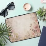 Soft beige laptop sleeve with delicate floral design in pink, green, and purple, featuring a zip closure for secure storage. the laptop sleeve on the table