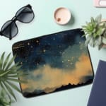 Laptop sleeve with a dark blue background featuring a starry night sky design with stars, clouds, and gradient effect. the laptop sleeve on the table