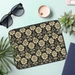 Infidu laptop sleeve with gold floral pattern on a black background. the laptop sleeve on the table