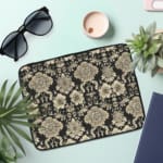 Laptop sleeve with elegant white floral and leaf motifs on a black background, featuring durable fabric and a secure zip closure. the laptop sleeve on the table