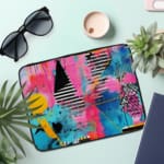 Laptop sleeve with a vibrant abstract design featuring blue, pink, purple, yellow, and black hues, secured with a zip closure. the laptop sleeve on the table