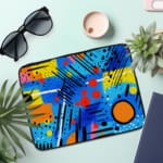 Laptop sleeve with a bright blue background featuring colorful abstract geometric shapes in yellow, pink, orange, black, and red, with zip closure. the laptop sleeve on the table