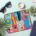 Laptop sleeve with a vibrant abstract design featuring shapes, lines, and patterns in blue, pink, yellow, and black. the laptop sleeve on the table