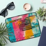 Infidu Colorful Abstract Laptop Sleeve featuring bright pink, blue, yellow, and black colors with stripes and dots on a vibrant design. the laptop sleeve on the table