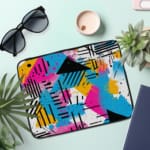 Infidu Modern Abstract Laptop Sleeve featuring bright colors like pink, blue, yellow, and black with geometric shapes and lines. the laptop sleeve on the table