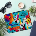 Infidu Vibrant Abstract Laptop Sleeve featuring bold colors like blue, orange, yellow, pink, and purple with geometric shapes and lines. the laptop sleeve on the table