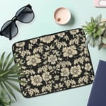 Infidu Black & Gold Floral Laptop Sleeve with a black background and detailed white floral pattern, featuring a secure zip closure. the laptop sleeve on the table