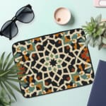 Infidu Traditional Geometric Laptop Sleeve with a bold multicolored pattern in white, black, orange, green, and blue on a dark background. the laptop sleeve on the table