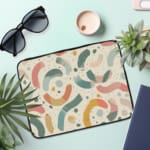 Colorful abstract laptop sleeve with curved shapes in pink, blue, yellow, and orange on a white background, the laptop sleeve on the table