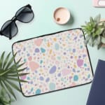 Terrazzo-style laptop sleeve with colorful spots in pink, blue, orange, and purple on a white background, The laptop sleeve covers the laptop