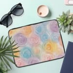 Laptop sleeve with a circular swirl pattern in pastel colors, including blue, pink, purple, yellow, and orange on a white background. the laptop sleeve on the table