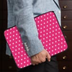 Pink laptop sleeve with a repeating white star pattern, shown against a bright background. the person holding the sleeve