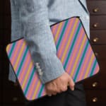 Colorful striped laptop sleeve with shades of blue, pink, yellow, and purple, offering a vibrant, playful design. the person holding the sleeve