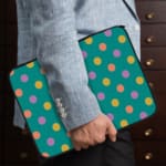 Playful pastel polka dot design laptop sleeve with yellow, purple, and orange dots on a teal background. the person holding the sleeve