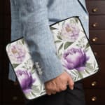 Elegant floral laptop sleeve with purple flowers and green leaves on a soft, light background. the person holding the sleeve