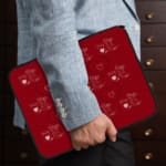 Red laptop sleeve with a playful white heart pattern on a bold red background, designed by digital artists for style and protection. the person holding the sleeve