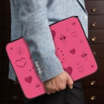 Infidu pink laptop sleeve with heart designs and dotted lines in shades of pink and purple. the person holding the sleeve