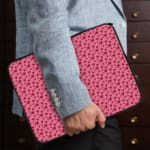 Pink laptop sleeve with a red heart pattern on a light surface. the person holding the sleeve