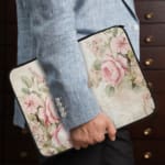 Elegant soft pink floral vintage laptop sleeve with light pink roses and green leaves on a pale background, designed for laptop protection. the person holding the sleeve