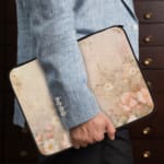 Beige laptop sleeve with subtle floral pattern, featuring a zip closure for secure protection. the person holding the sleeve