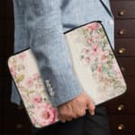 Soft beige laptop sleeve with delicate floral design in pink, green, and purple, featuring a zip closure for secure storage. the person holding the sleeve