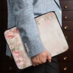 Soft beige laptop sleeve with delicate floral design in pink, green, and purple, featuring a zip closure for secure storage. the person holding the sleeve