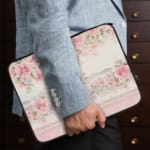 Floral laptop sleeve with pink and white flowers, black-bordered edges, soft background, and delicate floral design. the person holding the sleeve