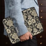 Laptop sleeve with elegant white floral and leaf motifs on a black background, featuring durable fabric and a secure zip closure. the person holding the sleeve