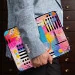 Infidu Bold Abstract Laptop Sleeve featuring bright geometric patterns in pink, blue, yellow, black, and white with a secure zip closure. the person holding the sleeve