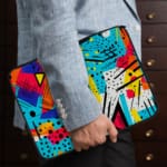 Infidu Vibrant Abstract Laptop Sleeve featuring bold colors like blue, orange, yellow, pink, and purple with geometric shapes and lines. the person holding the sleeve