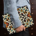 Infidu Traditional Geometric Laptop Sleeve with a bold multicolored pattern in white, black, orange, green, and blue on a dark background. the person holding the sleeve