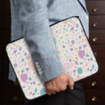 Terrazzo-style laptop sleeve with colorful spots in pink, blue, orange, and purple on a white background, the person holding the sleeve