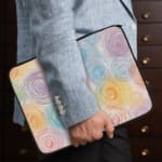 Laptop sleeve with a circular swirl pattern in pastel colors, including blue, pink, purple, yellow, and orange on a white background. the person holding the sleeve