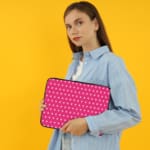 Pink laptop sleeve with a repeating white star pattern, shown against a bright background. the person holding the sleeve