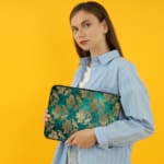 Elegant floral teal-blue laptop sleeve with beige and gold flowers, offering stylish protection for your laptop. the person holding the sleeve