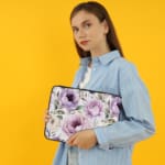 Infidu Elegant Purple Floral Laptop Sleeve featuring large purple flowers and green leaves on a light-colored background. the person holding the sleeve