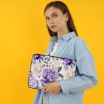 Elegant floral laptop sleeve with purple flowers and green leaves on a soft, light background. the person holding the sleeve