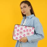 Light laptop sleeve with pink heart, ribbon, and beige mug pattern on a light background. the person holding the sleeve